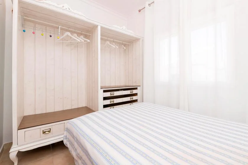 A bright bedroom with a striped bed beside open closets and drawers.