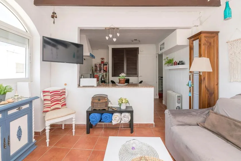 A bright living room with seating, a television, and an open kitchen area.
