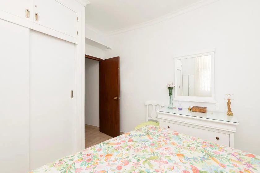 A bright bedroom with a floral bedspread and a white dresser beneath a mirror.