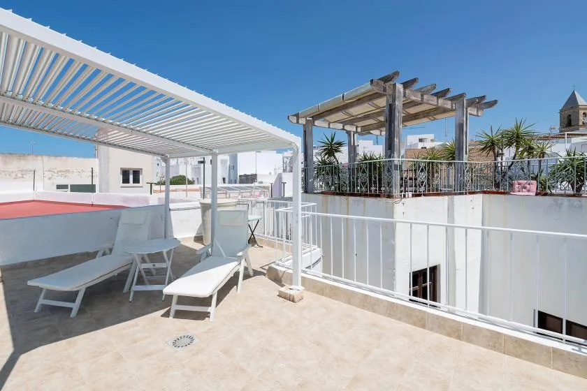 A sunny rooftop terrace with lounge seating, white pergolas, and potted plants.