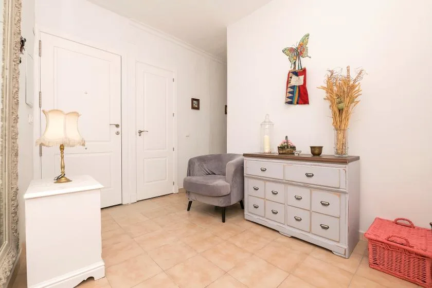 A bright entryway with a gray seat and a white dresser.