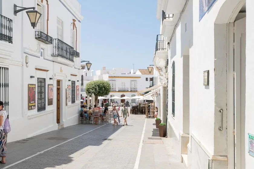 A sunny pedestrian street lined with white buildings and outdoor café seating.