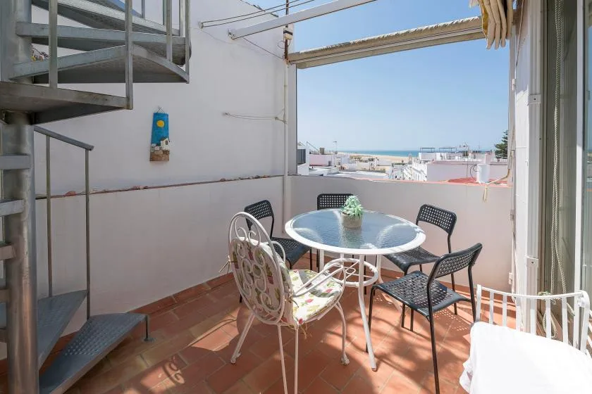A rooftop terrace with a round table and seating overlooking nearby buildings.