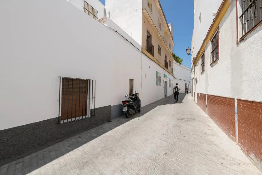 A narrow paved street runs between white buildings, with a scooter parked beside the wall.