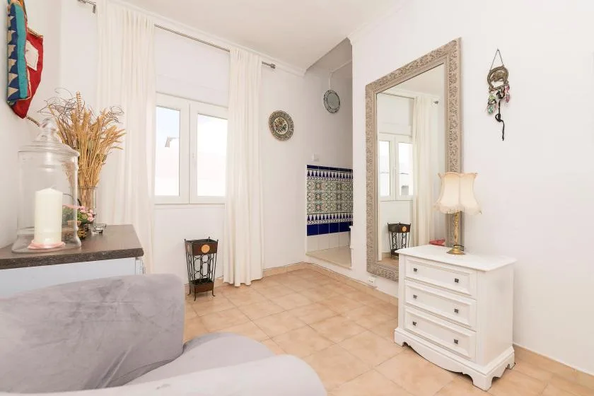 A bright living room with a large window, a mirror, and light-colored seating.