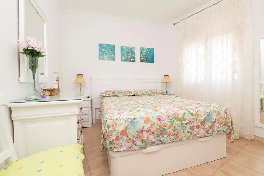 A bright bedroom with a bed covered in a colorful floral bedspread.