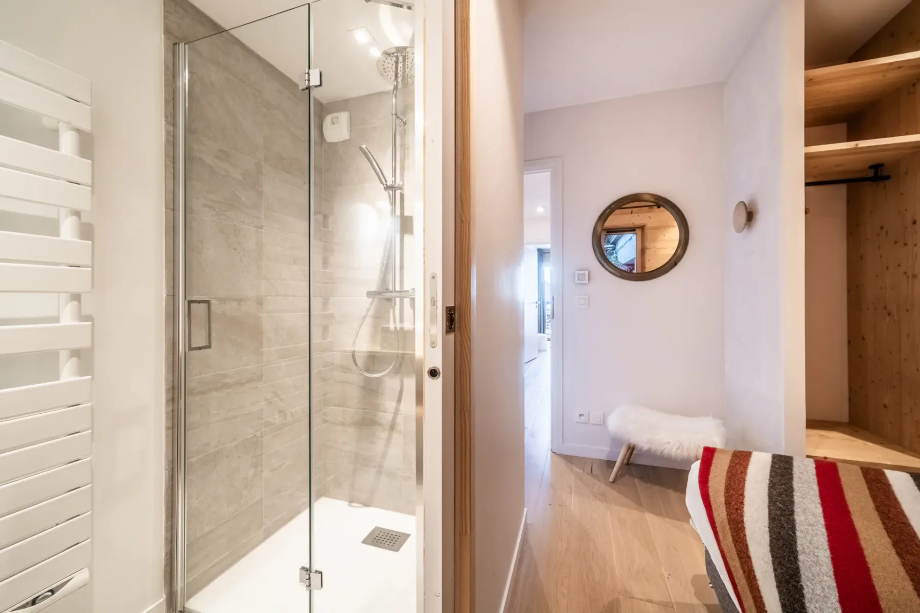 A bathroom with a glass shower, a round mirror, and a striped towel.