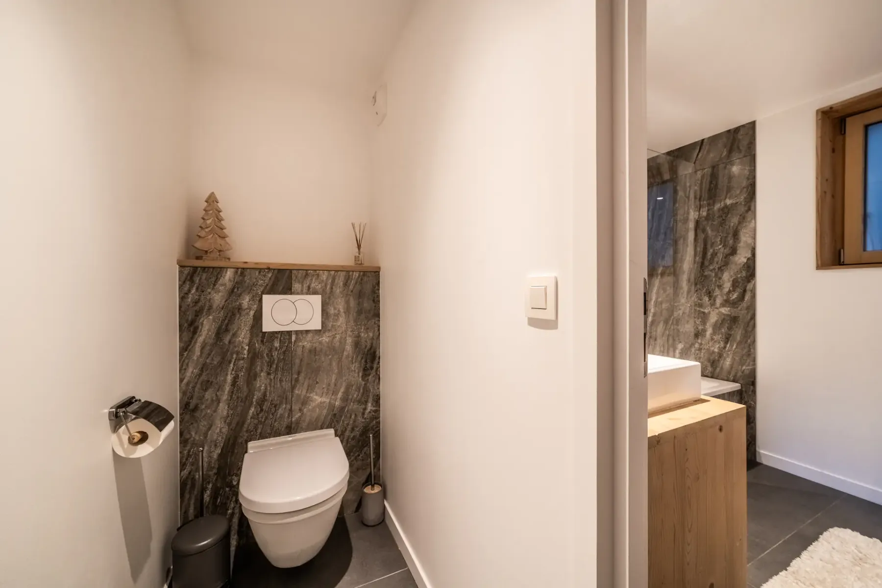A bathroom with a wall-mounted toilet and dark stone-patterned wall tiles.