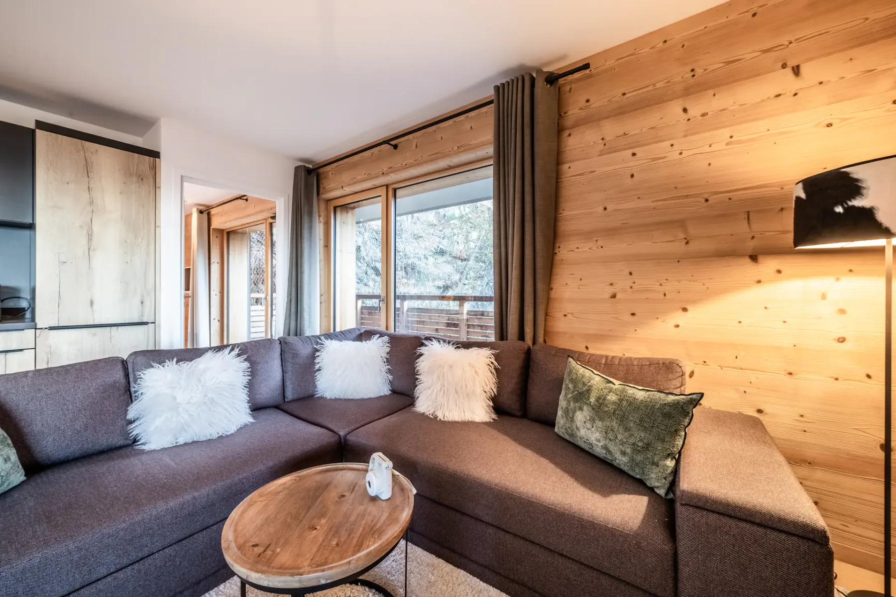 A living room with sectional seating beside large windows and wood-paneled walls.