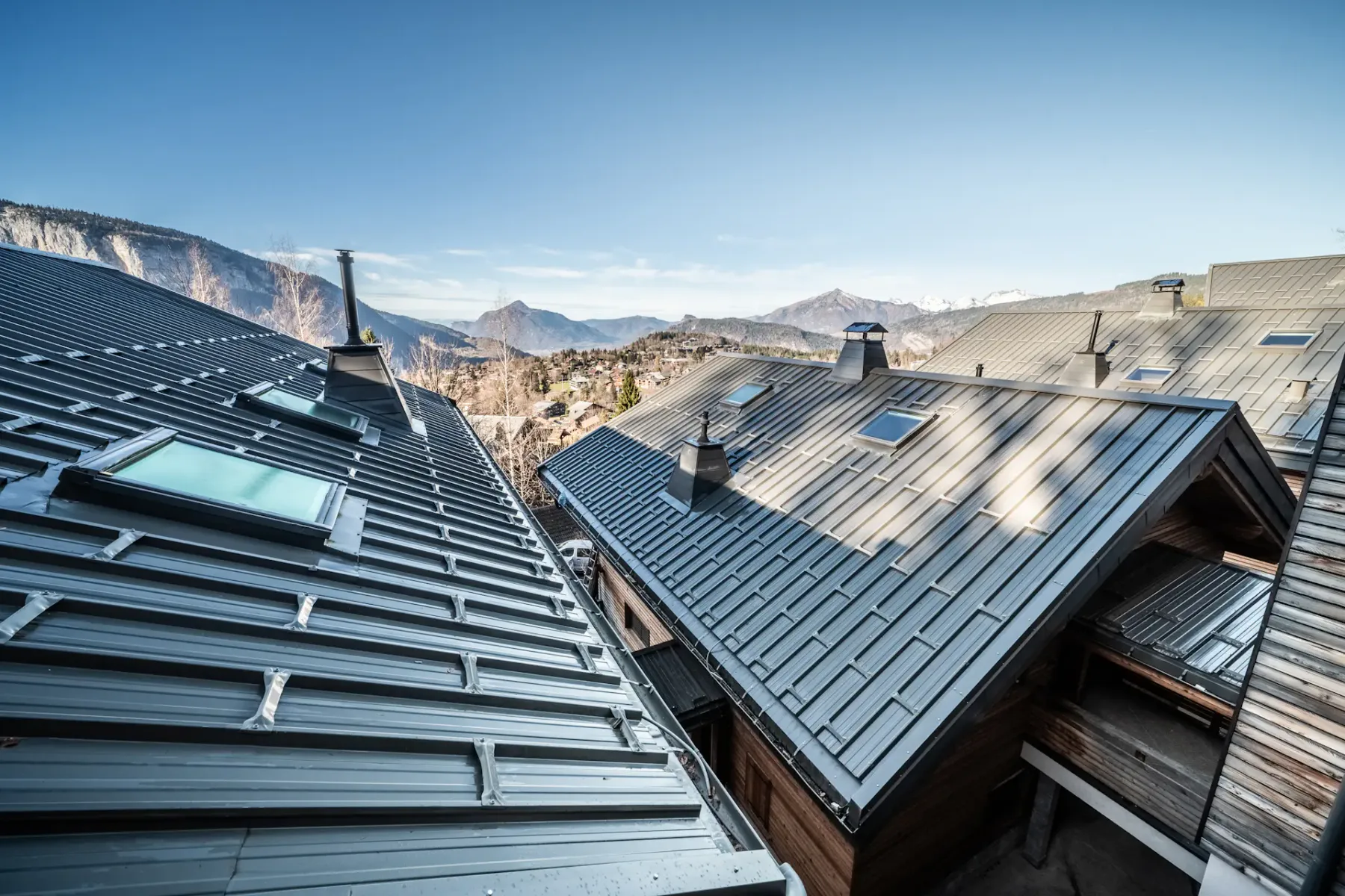 A view across several metal rooftops toward a mountain landscape under a clear sky.