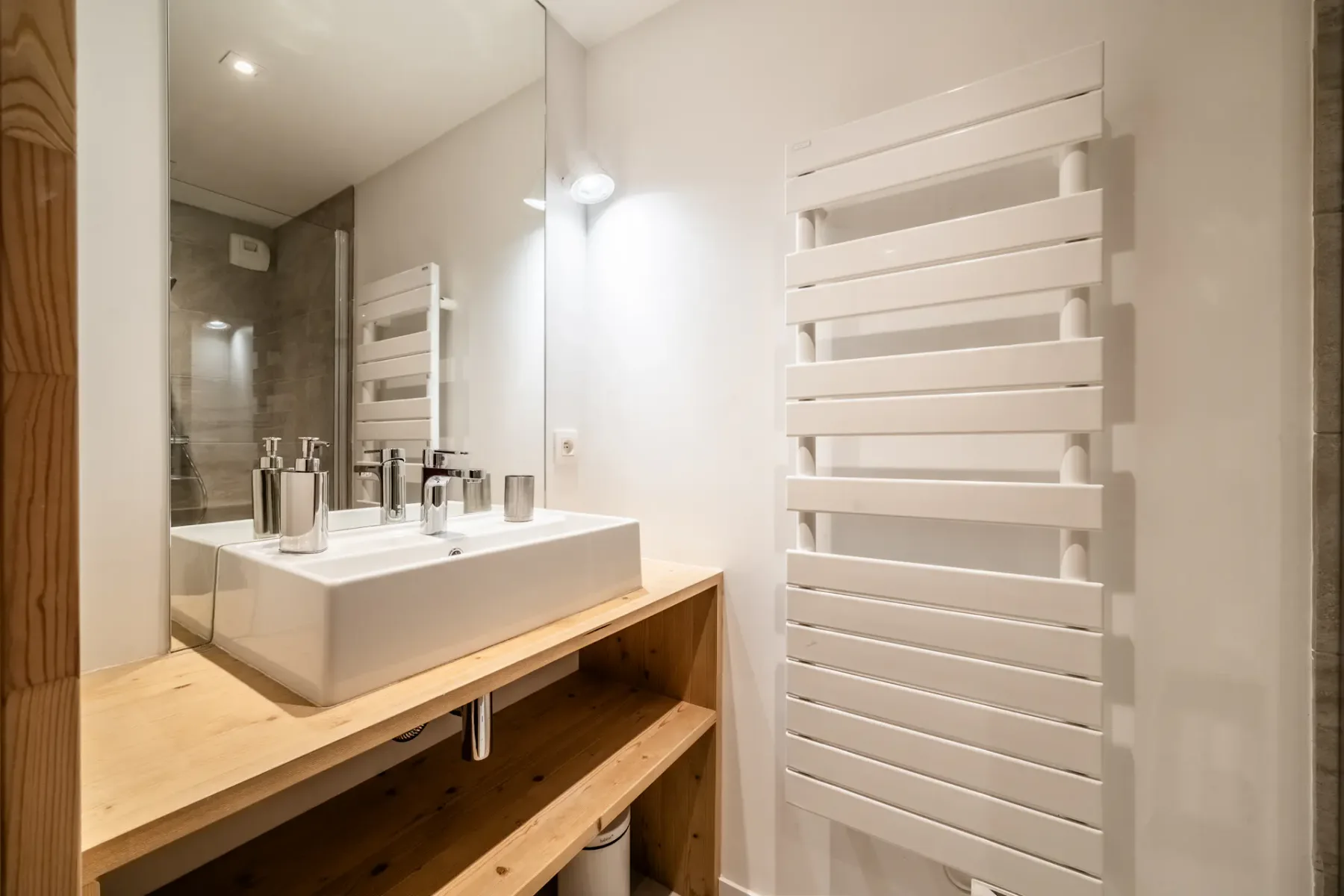 Modern bathroom with a white wall-mounted radiator, a rectangular sink on a wooden countertop, and a mirror under a ceiling light.