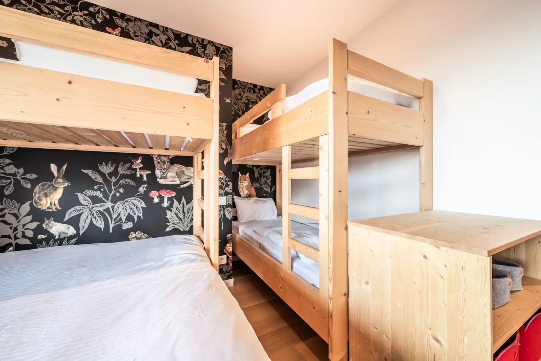 A bedroom with bunk beds, patterned wallpaper, and a wooden storage unit.