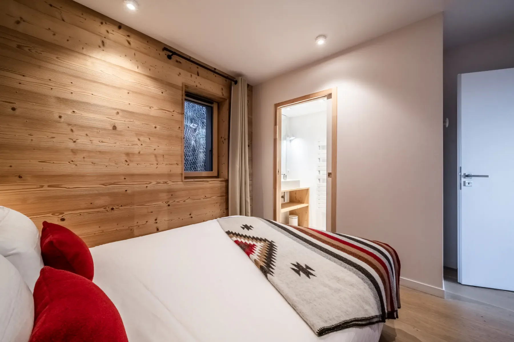 A bedroom with a bed, red pillows, and wood-paneled walls.