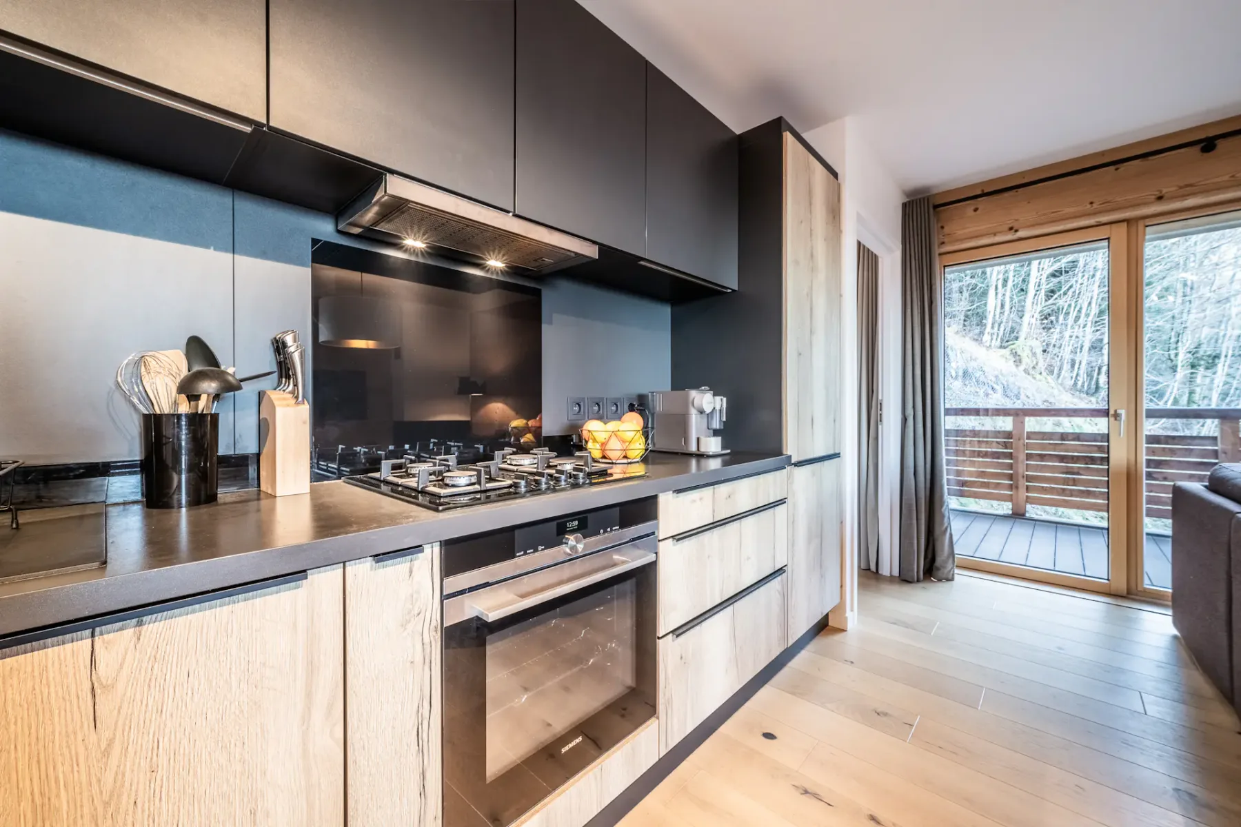 A modern kitchen with dark upper cabinets, a gas cooktop, and a sliding glass door.