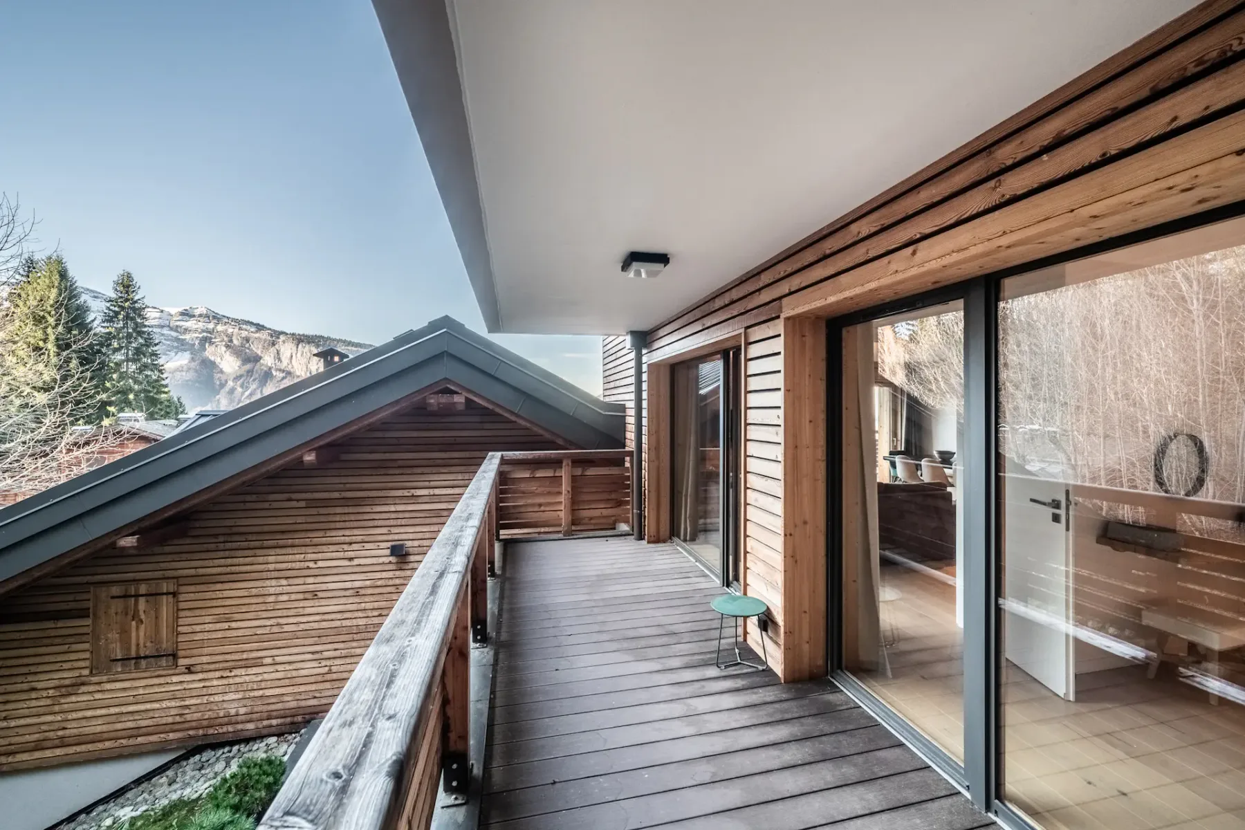 A covered wooden balcony runs alongside a building, with mountain scenery beyond the railing.