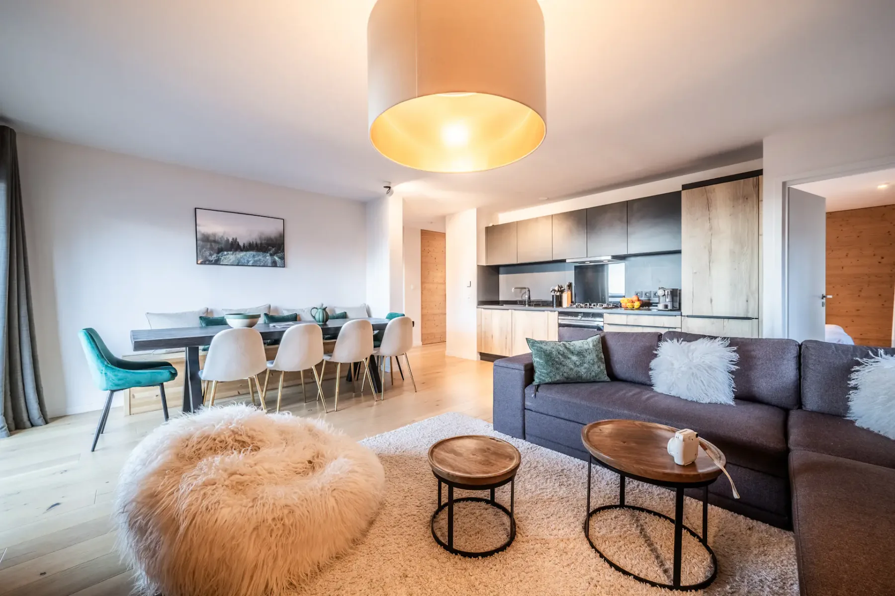 A living room with a gray sofa, round coffee tables, and an open kitchen and dining area.
