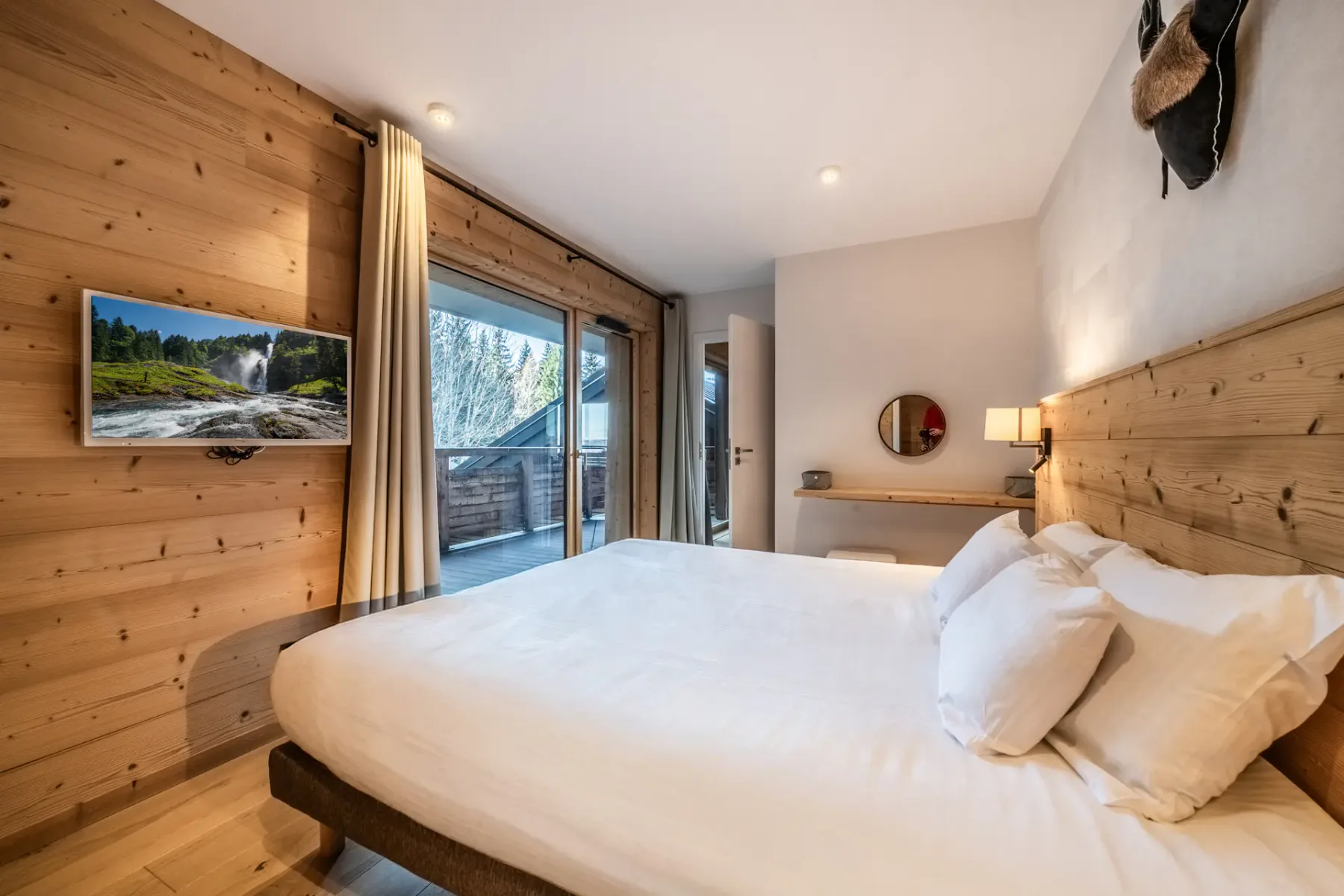 A bedroom with a white bed, wood-paneled walls, and sliding glass doors opening onto a balcony.