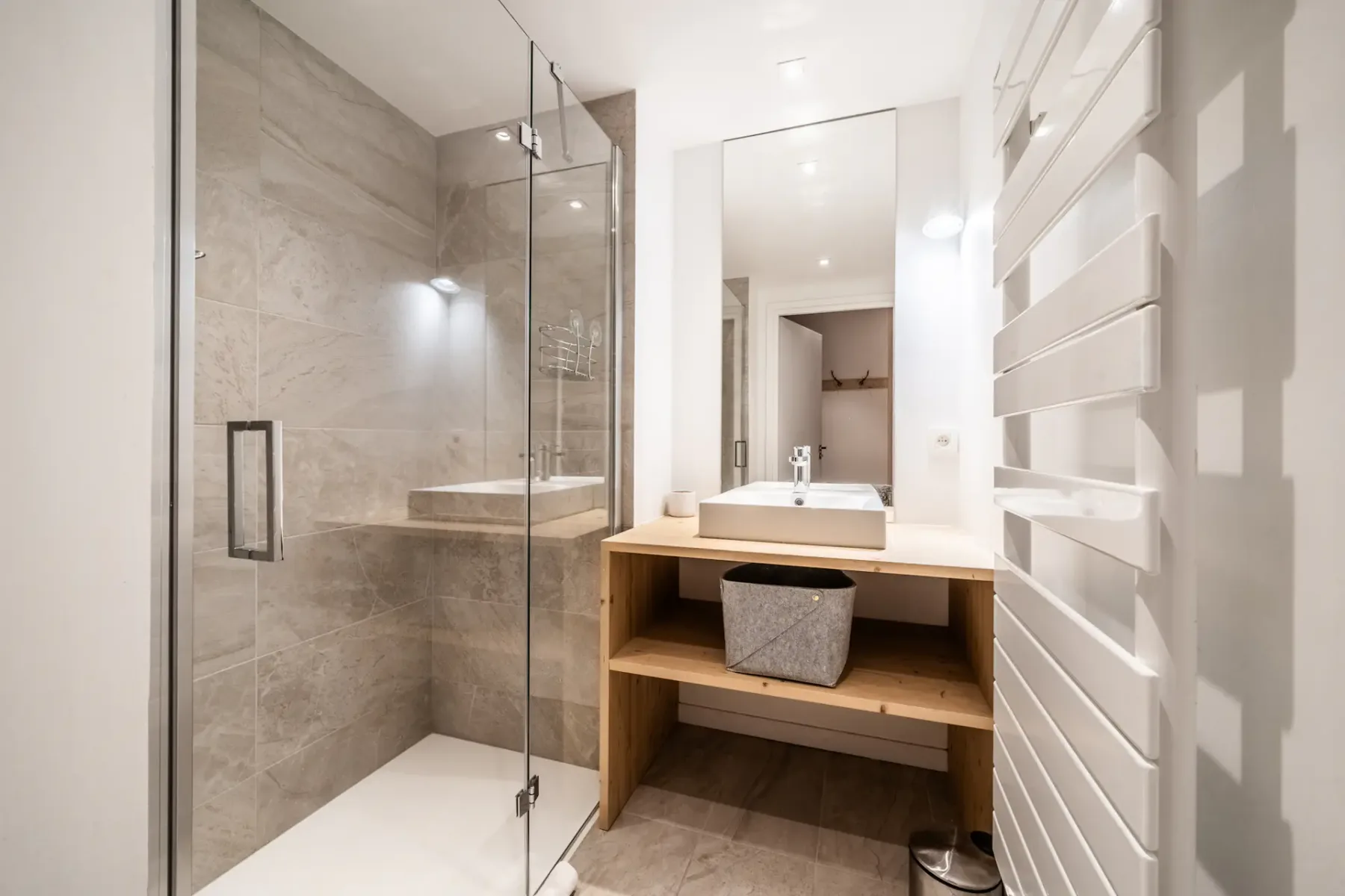Modern bathroom with a glass-enclosed shower, large mirror, rectangular sink on a wooden vanity, and a heated towel rack.