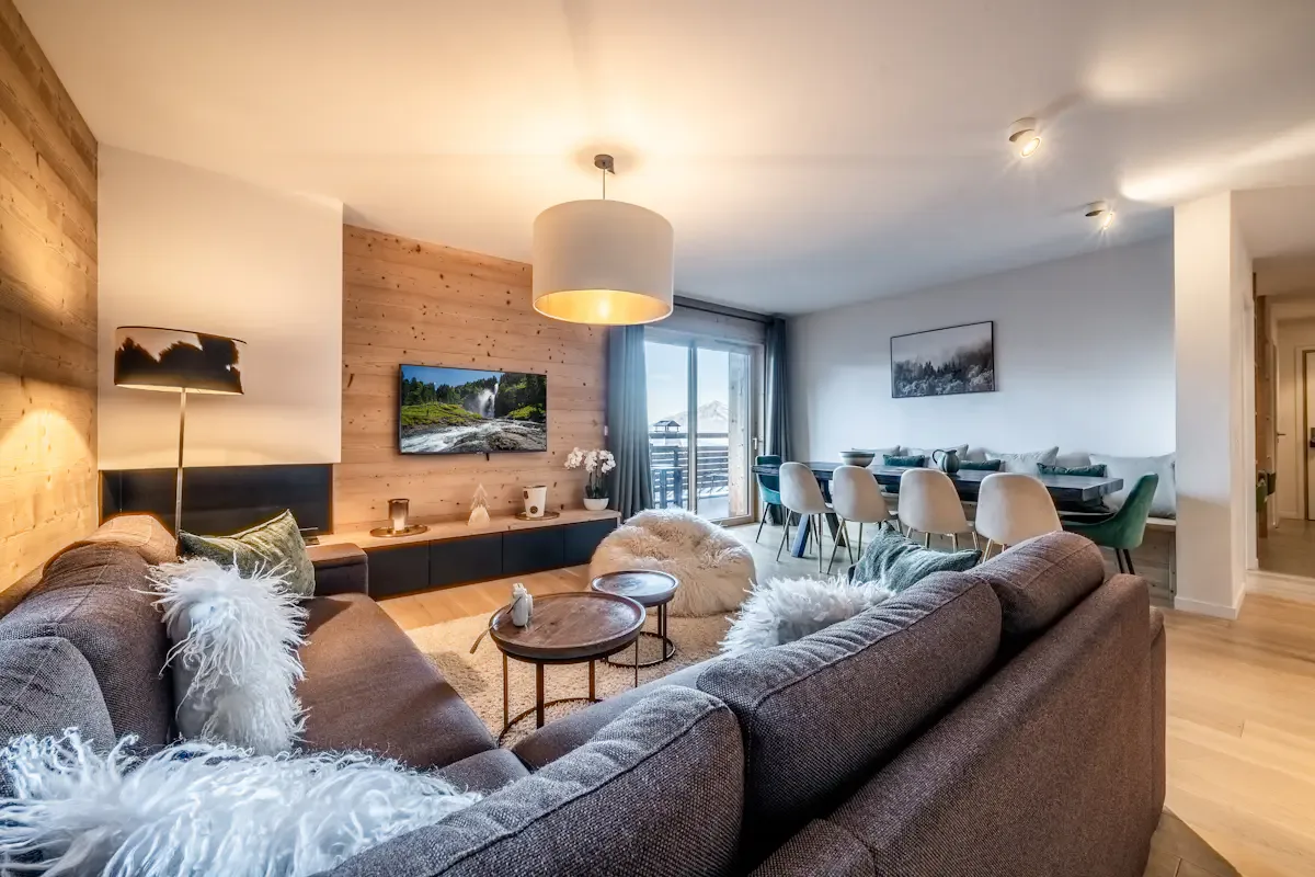 A living room with seating, a television, and a dining area by the windows.
