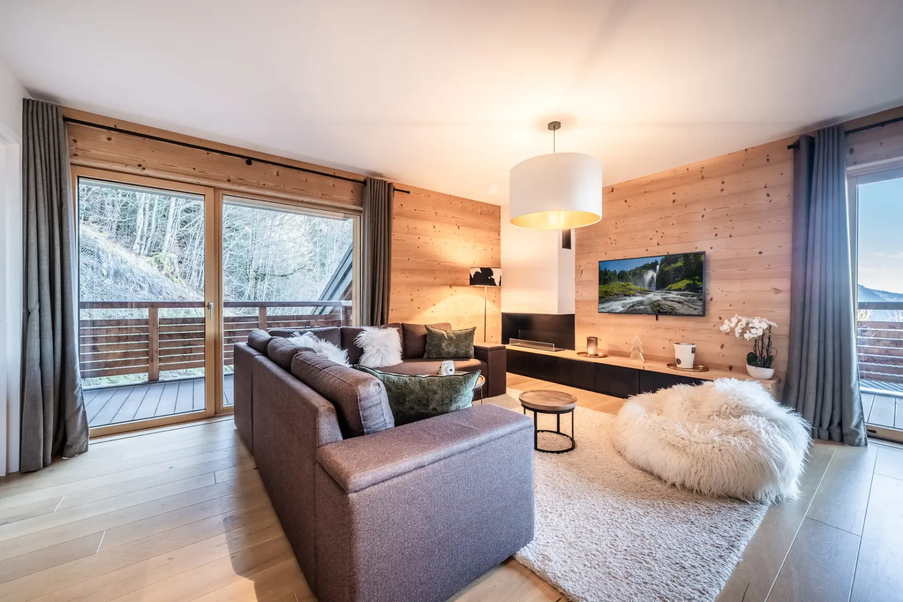 A wood-paneled living room with a sectional sofa, rug, and windows overlooking the outdoors.