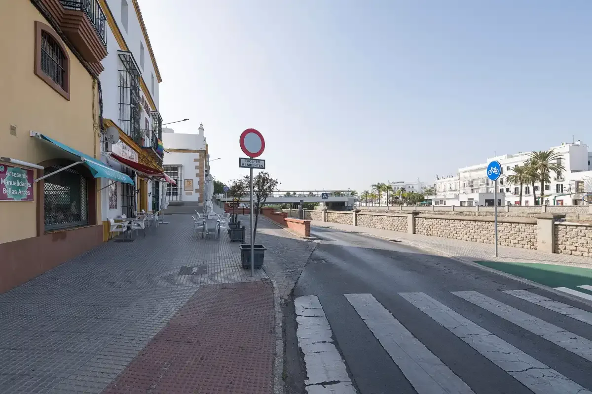 A street scene with a sidewalk, a pedestrian crossing, and low-rise buildings.