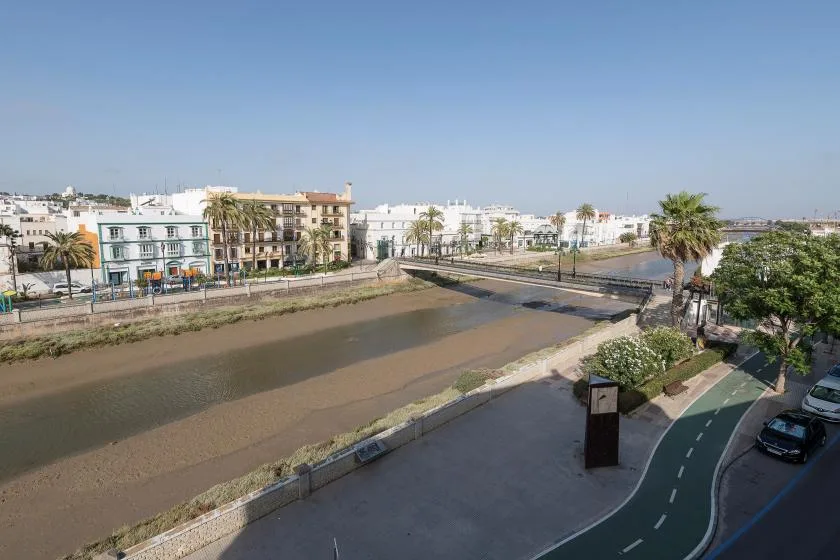 Urban streetscape beside a shallow waterway, with low-rise buildings and palm trees.