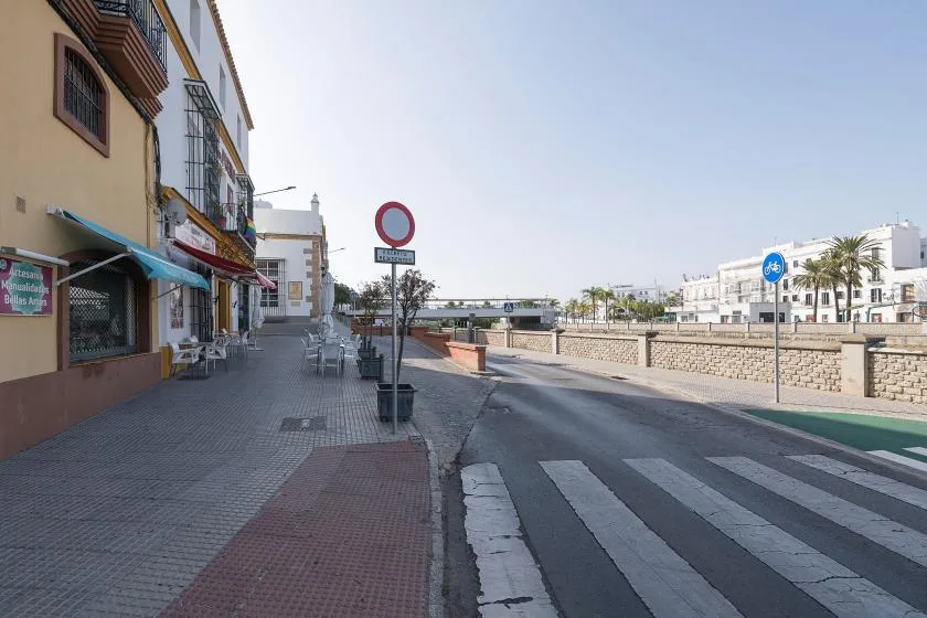 A paved street with a pedestrian crossing, low stone wall, and buildings.