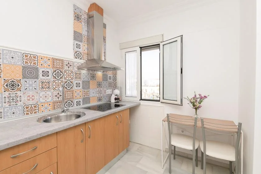 A bright kitchen with patterned backsplash, countertop seating, and a window.