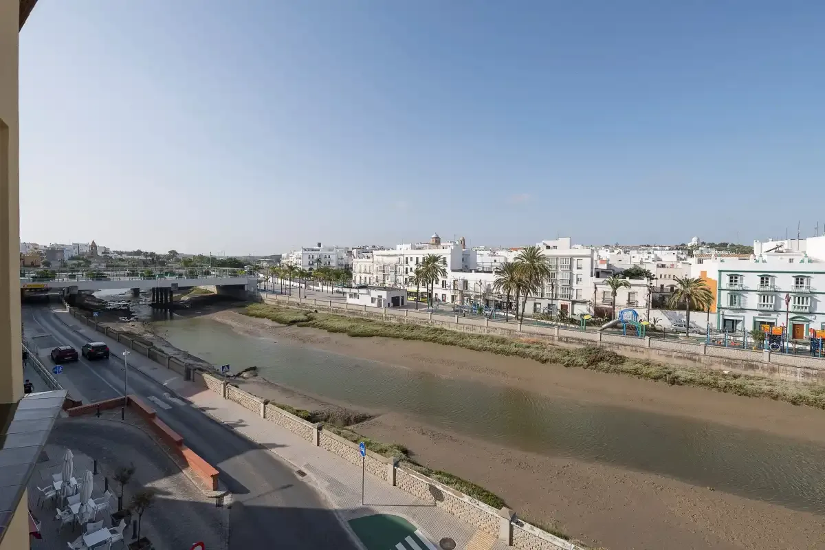 A river channel runs beside a road, with low-rise buildings beyond.