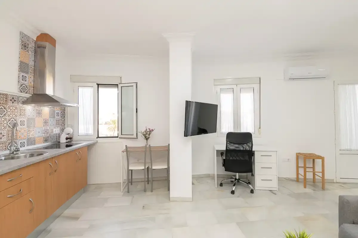 A bright open-plan room combines a kitchen, dining table, and desk area.