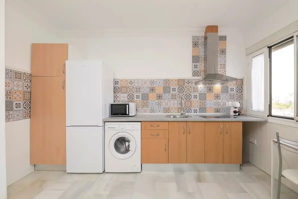 A bright kitchen with wooden cabinets, a refrigerator, and patterned tile backsplash.