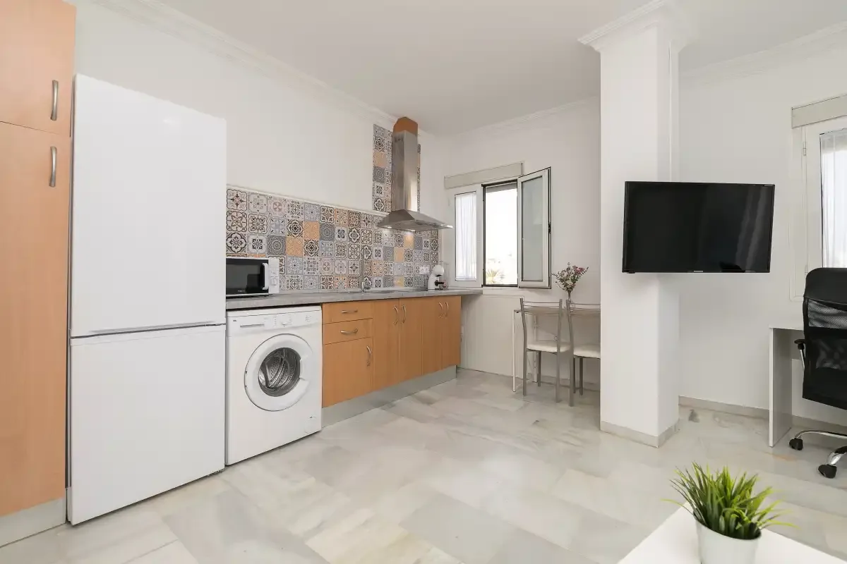 A bright kitchen and dining area with patterned backsplash tiles and a wall-mounted television.