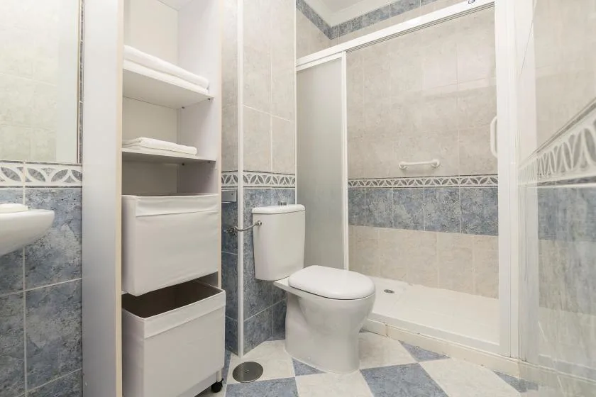 A tiled bathroom with a toilet, open shelving, and a shower area.