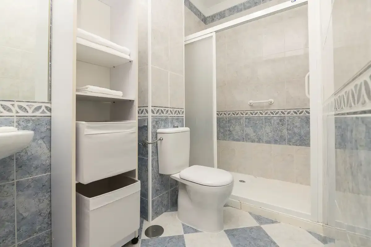 A bathroom with a toilet, storage shelves, and a shower.