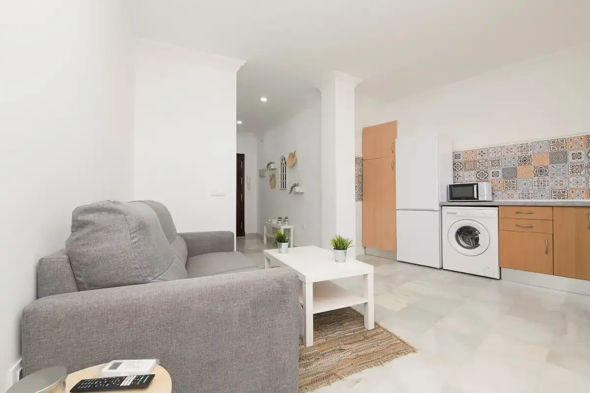 A bright living room opens onto a compact kitchen with light cabinetry.