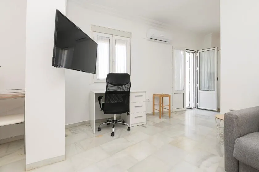 A bright room with a desk, office chair, wall-mounted television, and open glass doors.