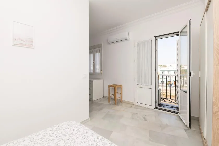 A bright bedroom with an open balcony door and a small bedside table.