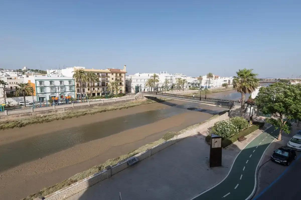 A riverside street scene with buildings, a bridge, and a marked cycle lane.