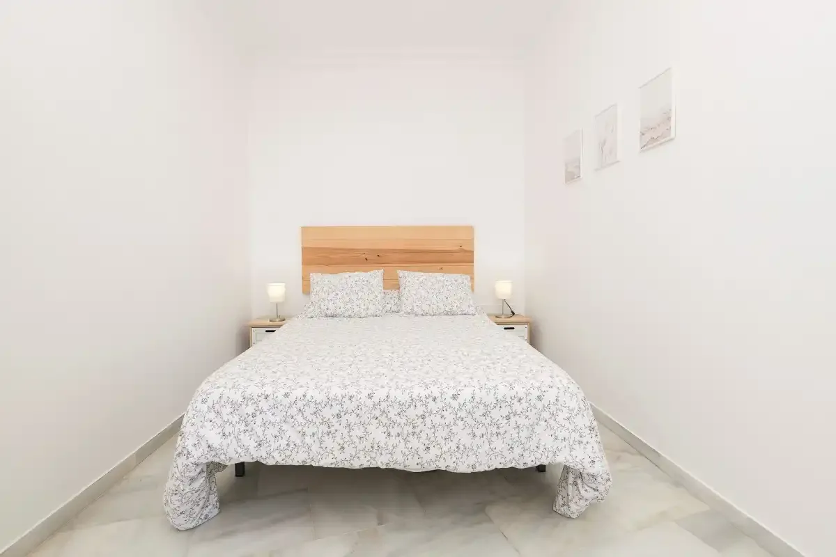 A bright bedroom with a double bed and wooden headboard.