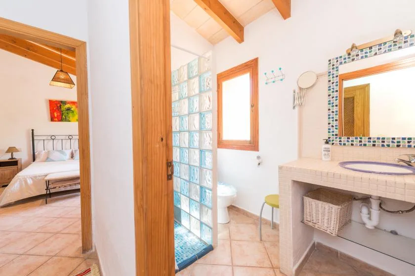 Un baño con ducha de bloques de vidrio, lavabo y ventana junto a un dormitorio.