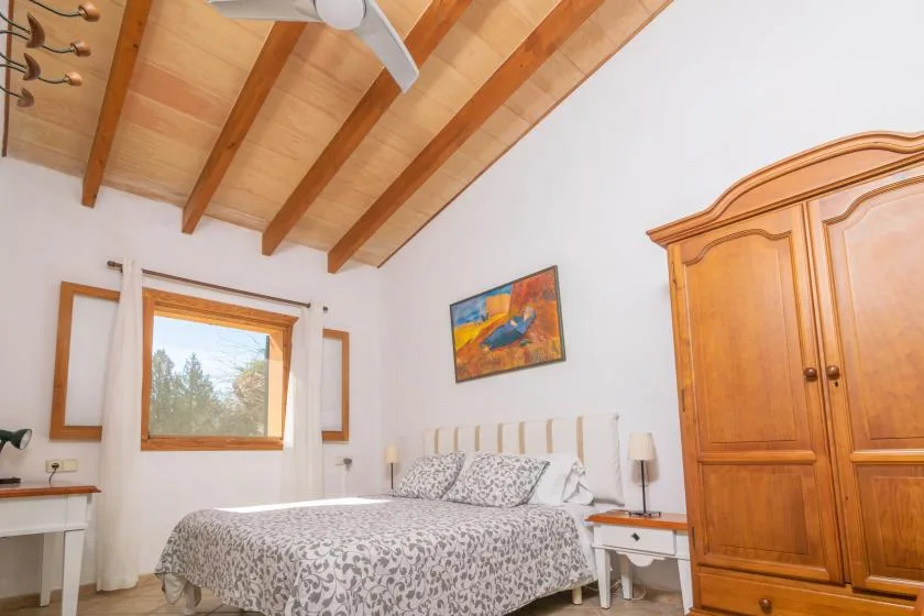 Un dormitorio con una colcha estampada, un armario de madera y vigas de techo expuestas.