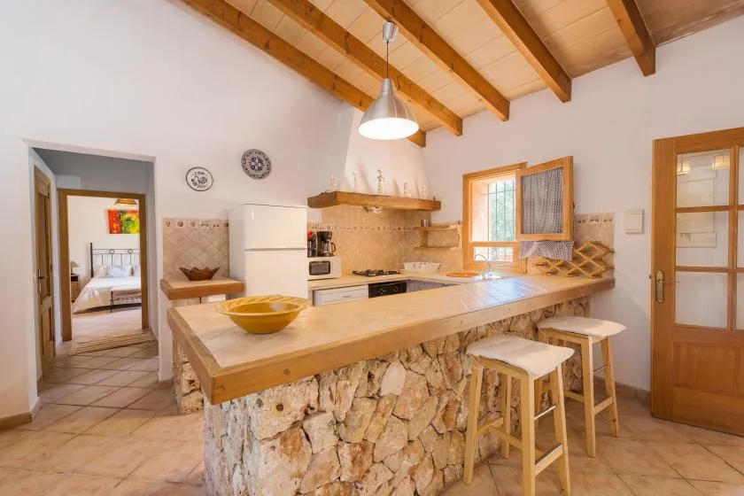 Una cocina con una isla larga, taburetes de madera y vigas de techo expuestas.