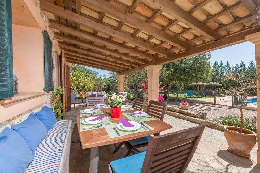 A covered outdoor dining area with a set table and seating beside a garden.