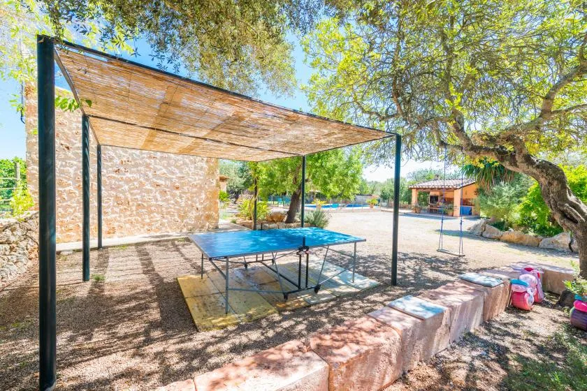 A shaded outdoor table tennis area sits beneath a canopy beside a stone wall.