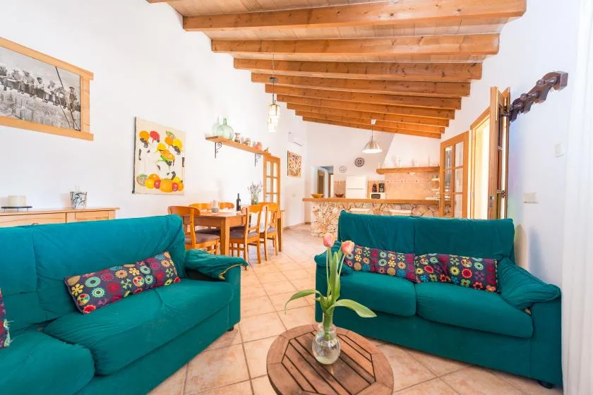Una sala de estar con asientos verde azulado, techo de madera y comedor al fondo.