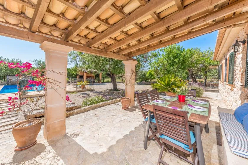 Una zona de comedor exterior a la sombra tiene una mesa de madera con platos y sillas.