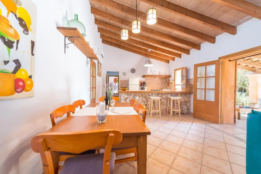 Comedor con una mesa de madera y una barra de cocina abierta bajo vigas vistas.
