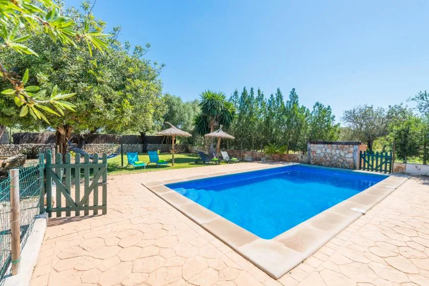 Una piscina al aire libre está junto a un patio pavimentado y asientos de jardín.