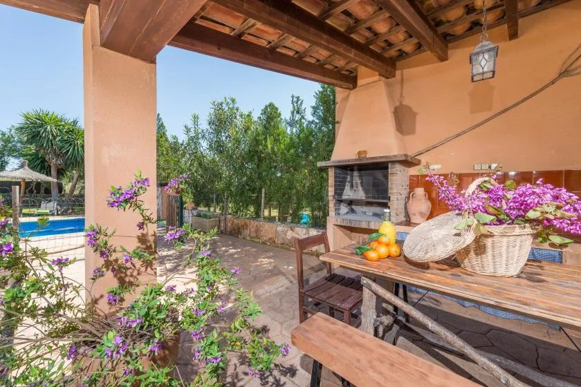A covered outdoor patio with a table, flowers, and a built-in grill.