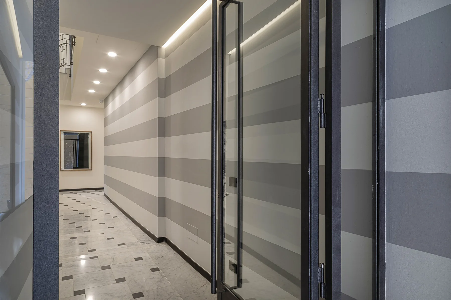 A striped hallway with a tiled floor and glass doors.